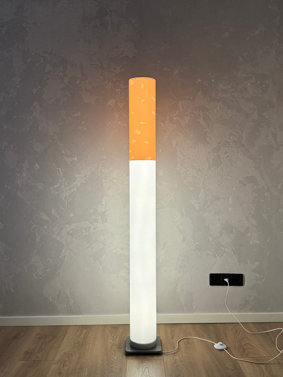 The Cigarette Lamp switched on — a 135 cm cigarette-shaped floor lamp glowing warm in a room corner